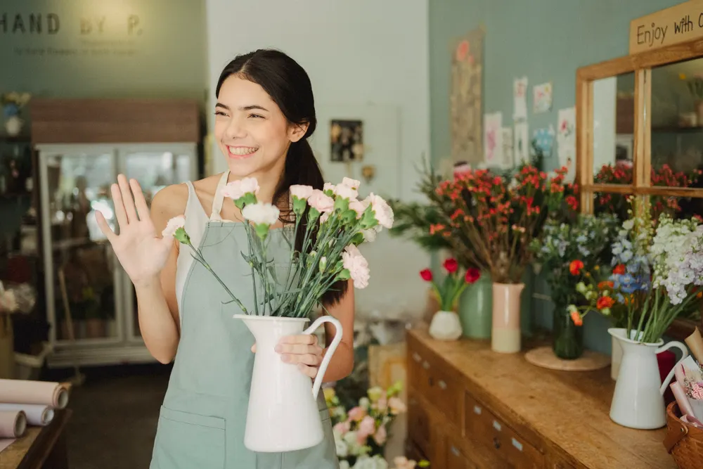 Smiling florist in an apron holding fresh flowers inside her shop