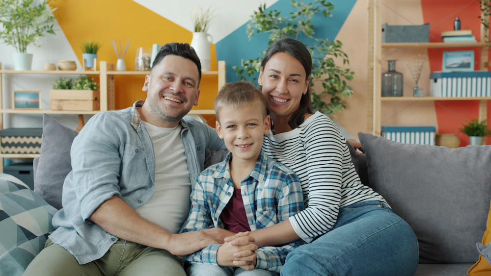 Parents and their son smiling together on the living room sofa