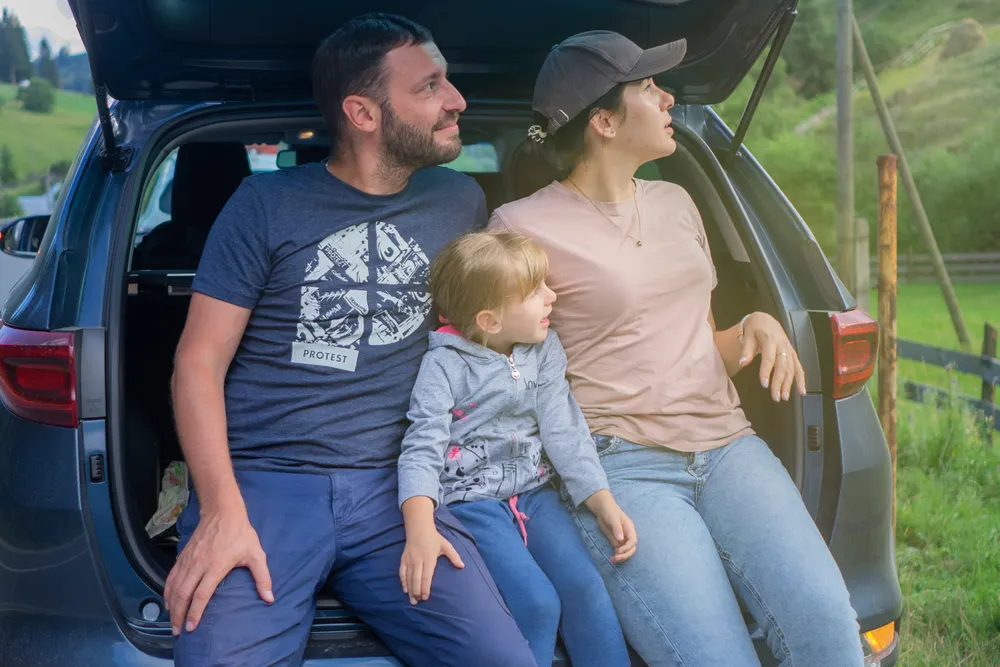 Parents and their young daughter sitting in the open back of their SUV